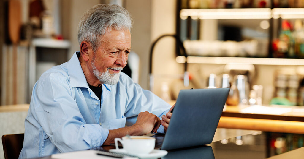 Retired U.S. expat smiling while researching Social Security benefits on a laptop over coffee, representing the planning challenges Americans abroad face with Social Security