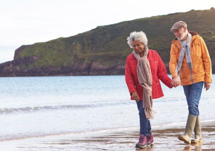 Senior couple holding hands and walking along shoreline.
