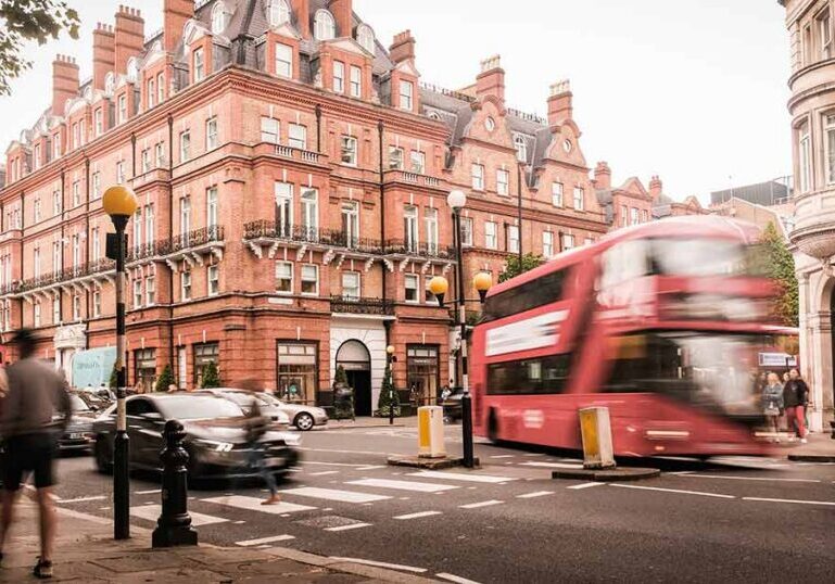 Luxury London street scene with red brick townhouses, double‑decker bus and pedestrians illustrating UHNW family neighborhoods and cross‑border wealth management in the UK.