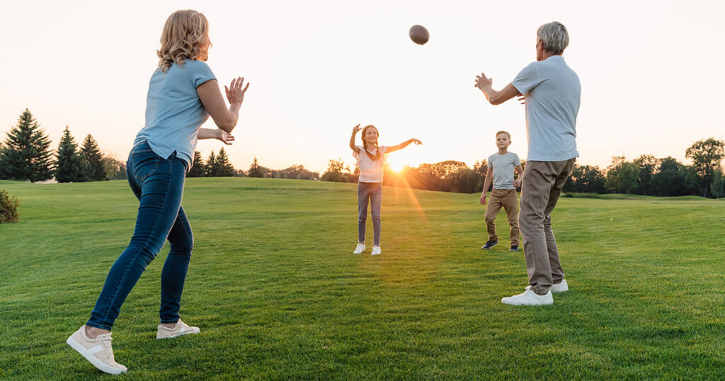Multigenerational family playing football together on a lawn at sunset, representing the lasting family wealth and shared values that family office investment services are designed to preserve and grow