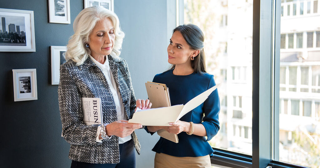 Senior female wealth advisor reviewing documents with a younger client in a high-rise office, representing tailored UHNW wealth management services for ultra-high-net-worth families