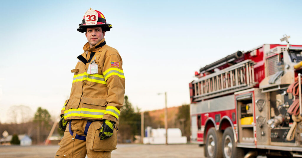 Firefighter captain standing in full gear in front of a fire truck, representing public safety employees who rely on a governmental 457b deferred compensation plan to bridge retirement income