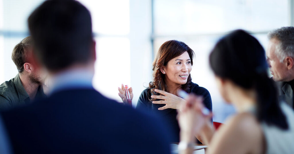 Professional woman leading a discussion with colleagues at a bright conference table, representing the collaborative guidance available to beginners starting their retirement planning journey