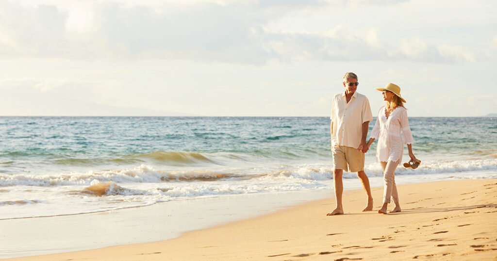 Married couple walking hand in hand along a sunny Florida beach, representing the estate planning and tax benefits a Florida Community Property Trust can offer married couples