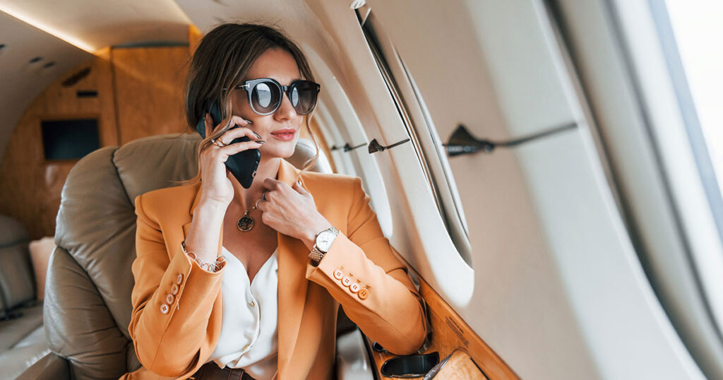 Affluent woman talking on the phone aboard a private jet, representing the lifestyle and complex wealth management needs of an ultra-high-net-worth individual