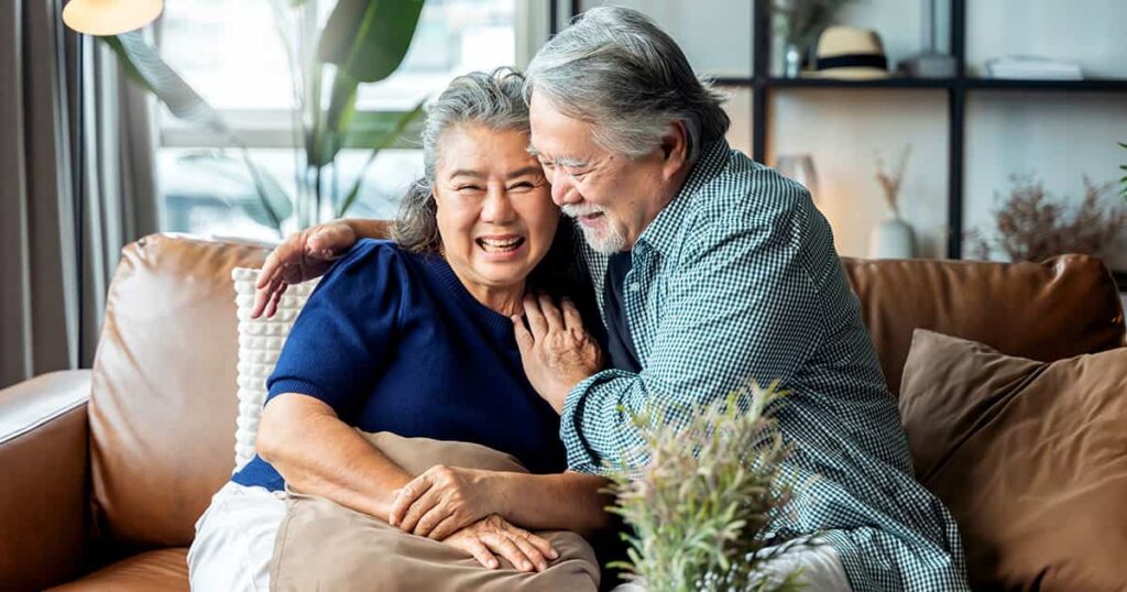 A happy retired couple laughing together on a couch in a comfortable, modern home.