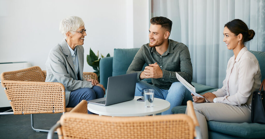 Young couple meeting with a senior female financial advisor in a modern lounge setting, representing affluent families beginning to explore family office finance, governance and multigenerational wealth planning