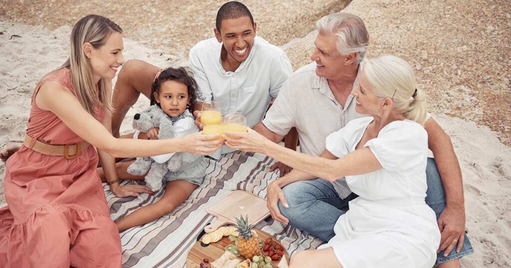 Multigenerational family sharing a beach picnic and toasting together, symbolizing how thoughtful family office structures support wealth, governance and harmony across generations
