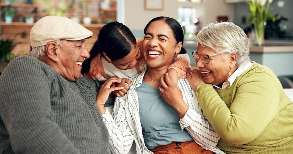 A happy multi-generational family—grandparents, mother, and young daughter—laughing and hugging together on a sofa at home