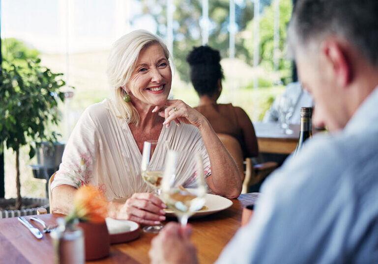 Older couple enjoying a relaxed meal together at a restaurant with glasses of white wine.