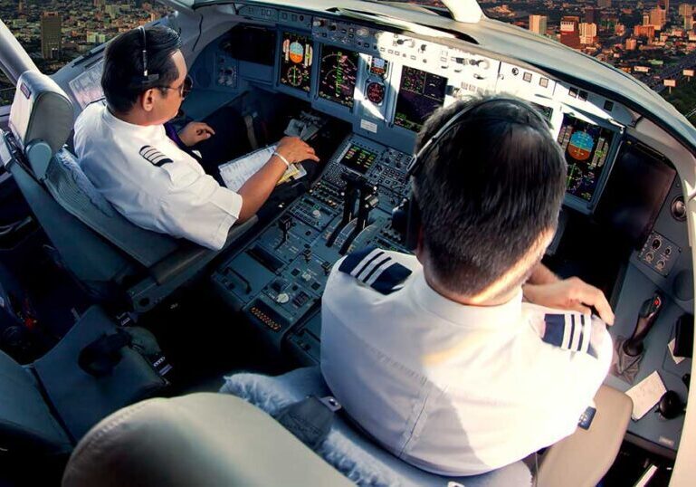 Two pilots in an airline cockpit during flight, with a city visible below