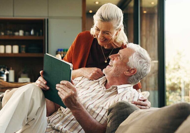 Retired couple relaxing together at home while reviewing information on a tablet, representing high-net-worth families using comprehensive estate planning to protect their legacy