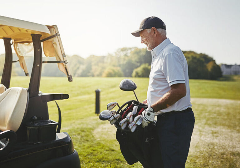 Retiree standing beside a golf cart and holding a bag of clubs on a sunny course, representing an active lifestyle and healthy habits that support a fulfilling retirement
