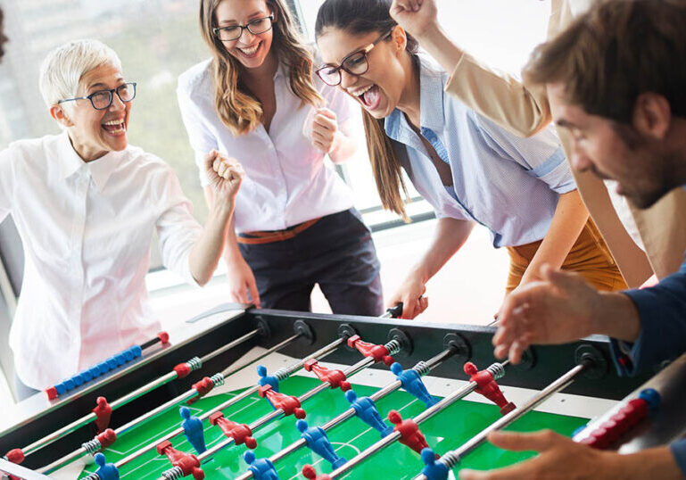 Coworkers of various ages work together playing foosball