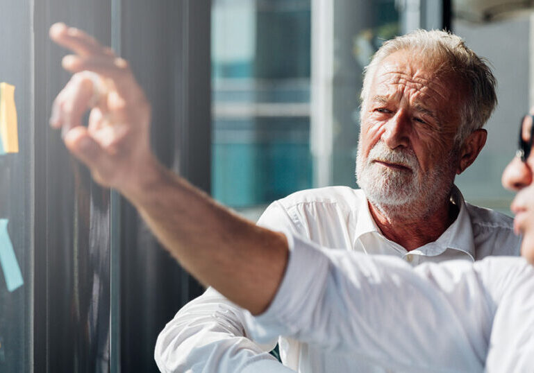 Two older professionals reviewing plans on a glass wall, representing how today’s millionaires take a more active, strategic approach to designing their retirement lifestyle