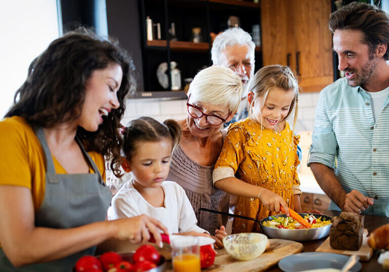 Multigenerational family preparing a meal together in the kitchen, representing coordinated family office risk management strategies to protect and preserve family wealth across generations