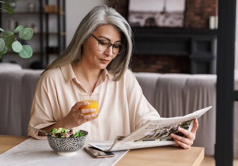 Middle-aged woman reading newspaper over breakfast while thinking about economic and political uncertainty