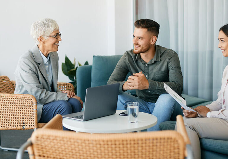 Young couple meeting with a senior female financial advisor in a modern lounge setting, representing affluent families beginning to explore family office finance, governance and multigenerational wealth planning