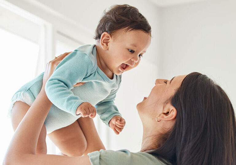 Parent holding up smiling baby at home to symbolize saving and investing for a child’s future.