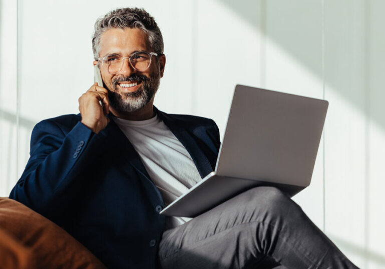 Ultra-high-net-worth individual sitting with a laptop and talking on the phone, representing customized family office-style services that coordinate complex wealth, planning and governance