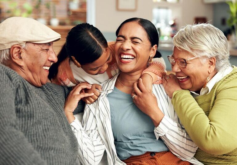 A happy multi-generational family—grandparents, mother, and young daughter—laughing and hugging together on a sofa at home