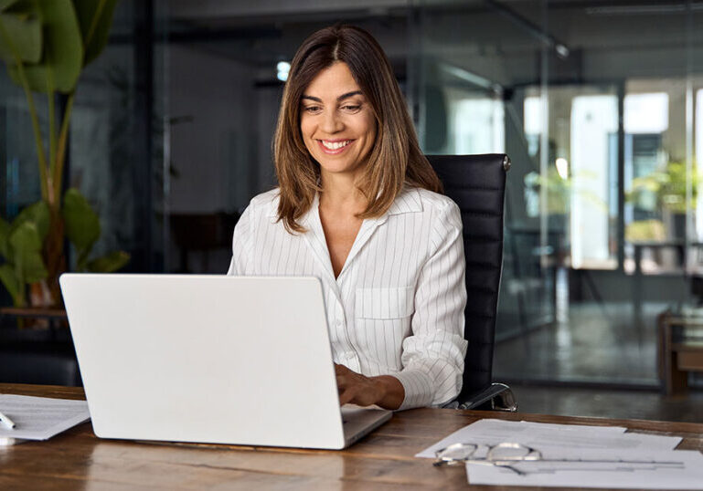Smiling business owner working on a laptop in a modern office, representing tips for building an accounting software tech stack to streamline bookkeeping and financial management