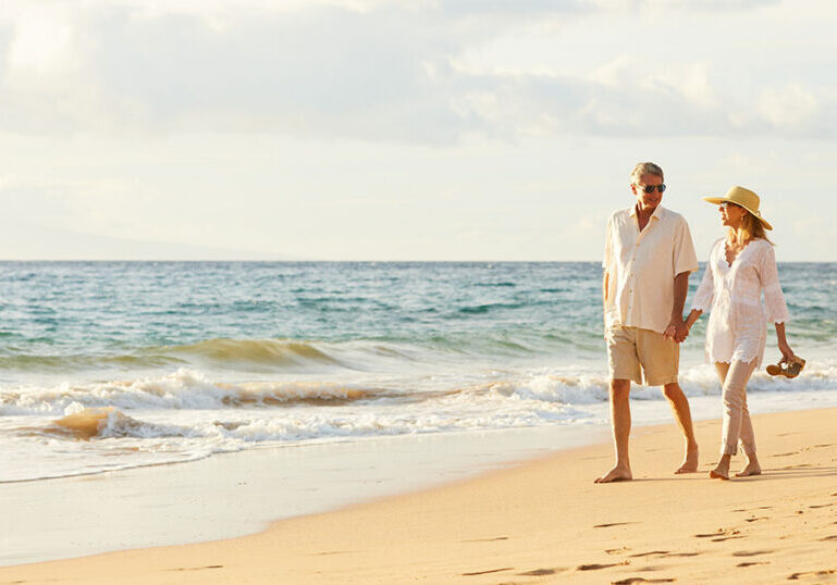 Married couple walking hand in hand along a sunny Florida beach, representing the estate planning and tax benefits a Florida Community Property Trust can offer married couples