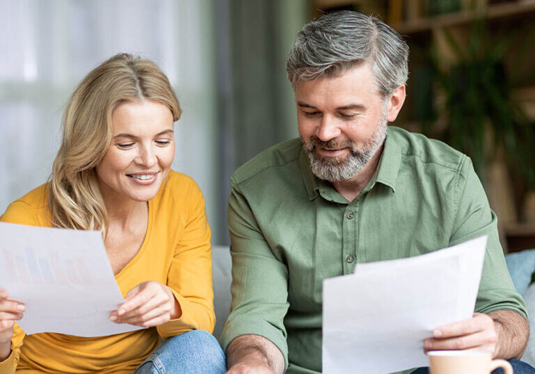Happy middle aged spouses checking financial documentation and calculating spents while planning family budget together at home, smiling mature spouses reading papers and using calculator