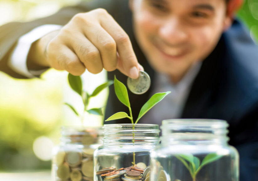 Businessman putting coin into the glass jar with young plant, demonstrating financial growth through saving plans and investment schemes