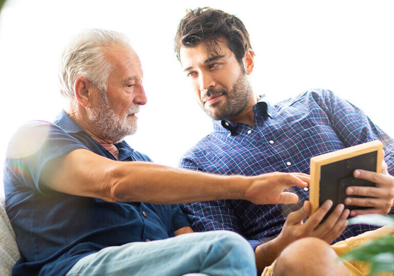 Father and son family time together at home concept. Happy old father and son sitting together and looking photos while remembering old times past.