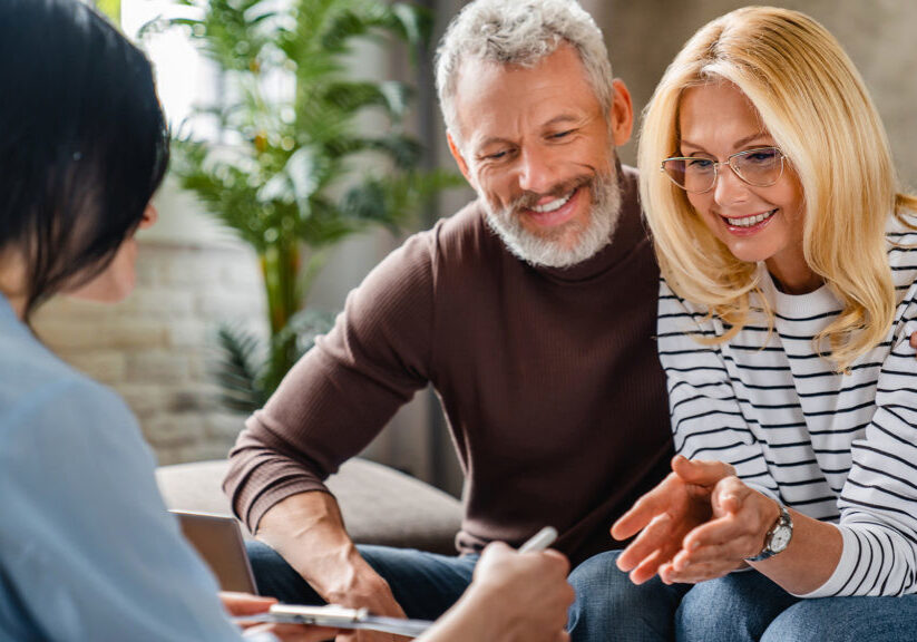Estate agent or financial adviser showing terms of contract to happy couple on notepad