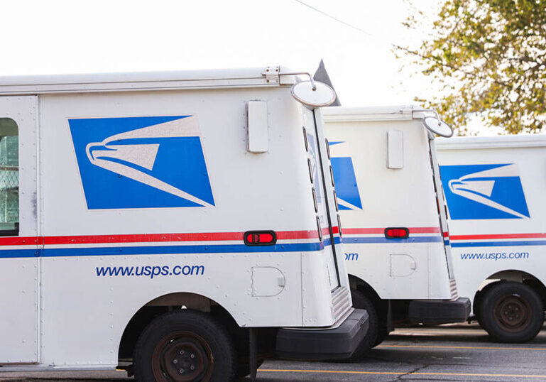 USPS mail delivery trucks parked in a row with official blue and red logo